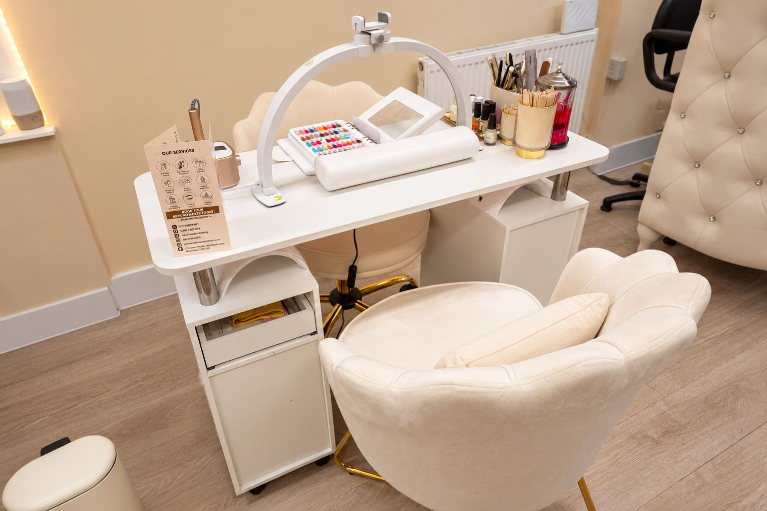 A white nail station with a gold lamp and a cream shell-back chair