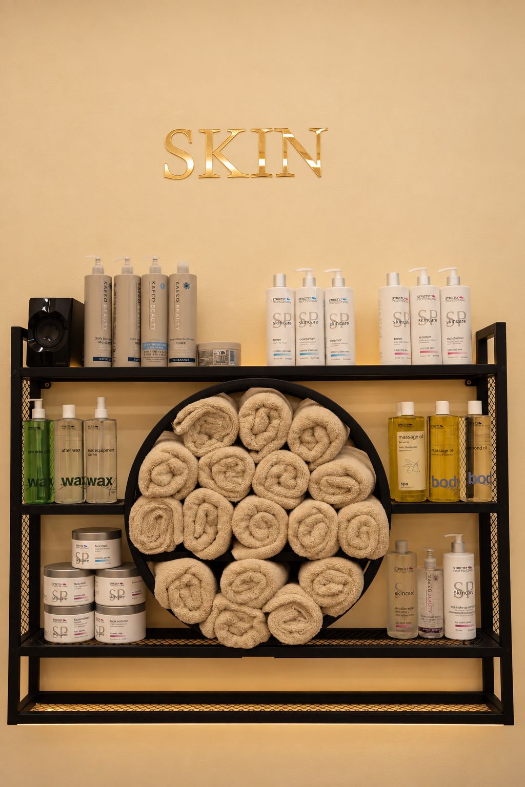 Rolled cream towels and skincare products on a shelf beneath gold Skin lettering
